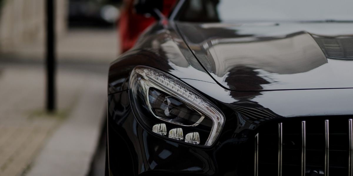 Close-up view of the front of a glossy black luxury sports car, highlighting its intricate LED headlight and reflective hood