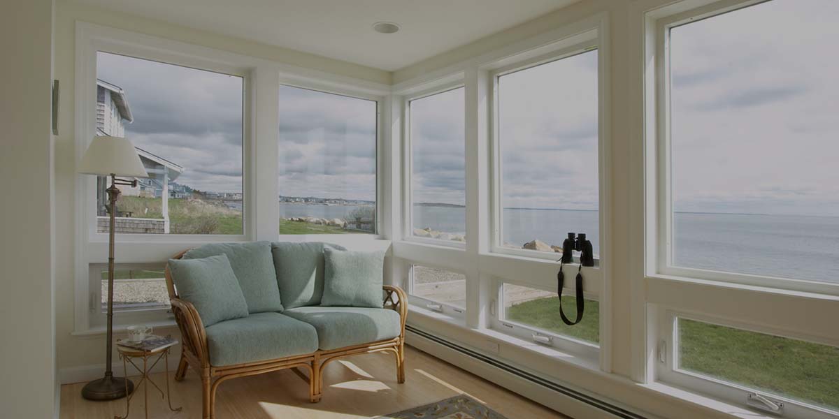 A sun-filled room features a light blue wicker loveseat facing large windows with a scenic view of the ocean