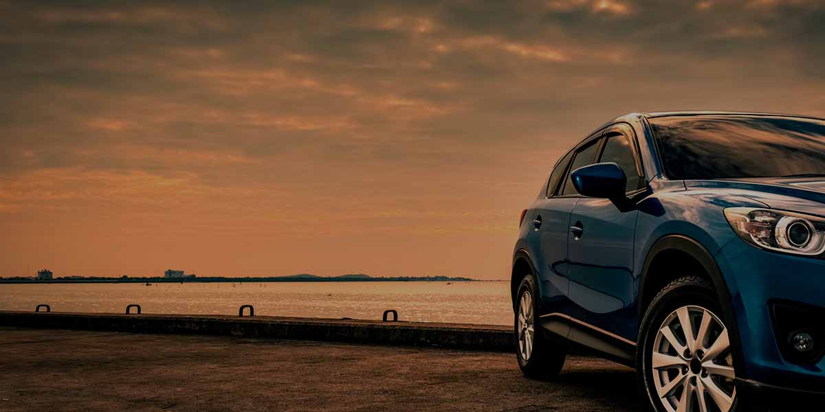 A blue SUV parked on a pier overlooking a calm body of water under a warm, golden sunset sky